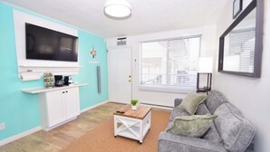 A living room with a TV, sofa, coffee table, and a window with blinds. - Mirabella 1D-Oceanside 122nd St, AC, Free WiFi. (Ocean City)