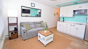 A compact living space with a sofa, a small wooden table, a kitchenette, and a mirror on the wall. - Mirabella 1D-Oceanside 122nd St, AC, Free WiFi. (Ocean City)