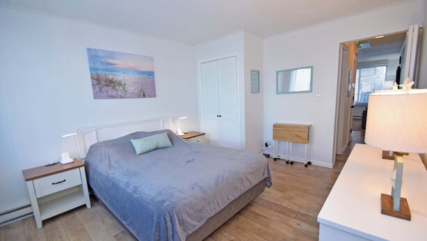 A bedroom with a bed, bedside tables, a nightstand, a lamp, a mirror, and a door leading to another room. - Mirabella 1D-Oceanside 122nd St, AC, Free WiFi. (Ocean City)