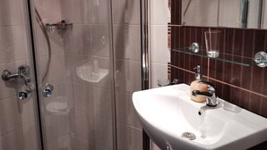 Une salle de bain avec une douche à parois de verre, un lavabo blanc doté d’un porte-savon en bois et une étagère en verre au-dessus du lavabo.