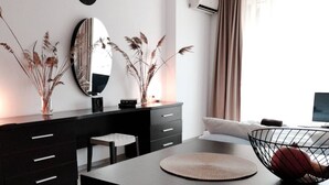 Un salon moderne avec une table à manger noire, un canapé noir et un grand miroir au mur. Il y a une fenêtre avec des rideaux et un appareil de climatisation fixé au mur.
