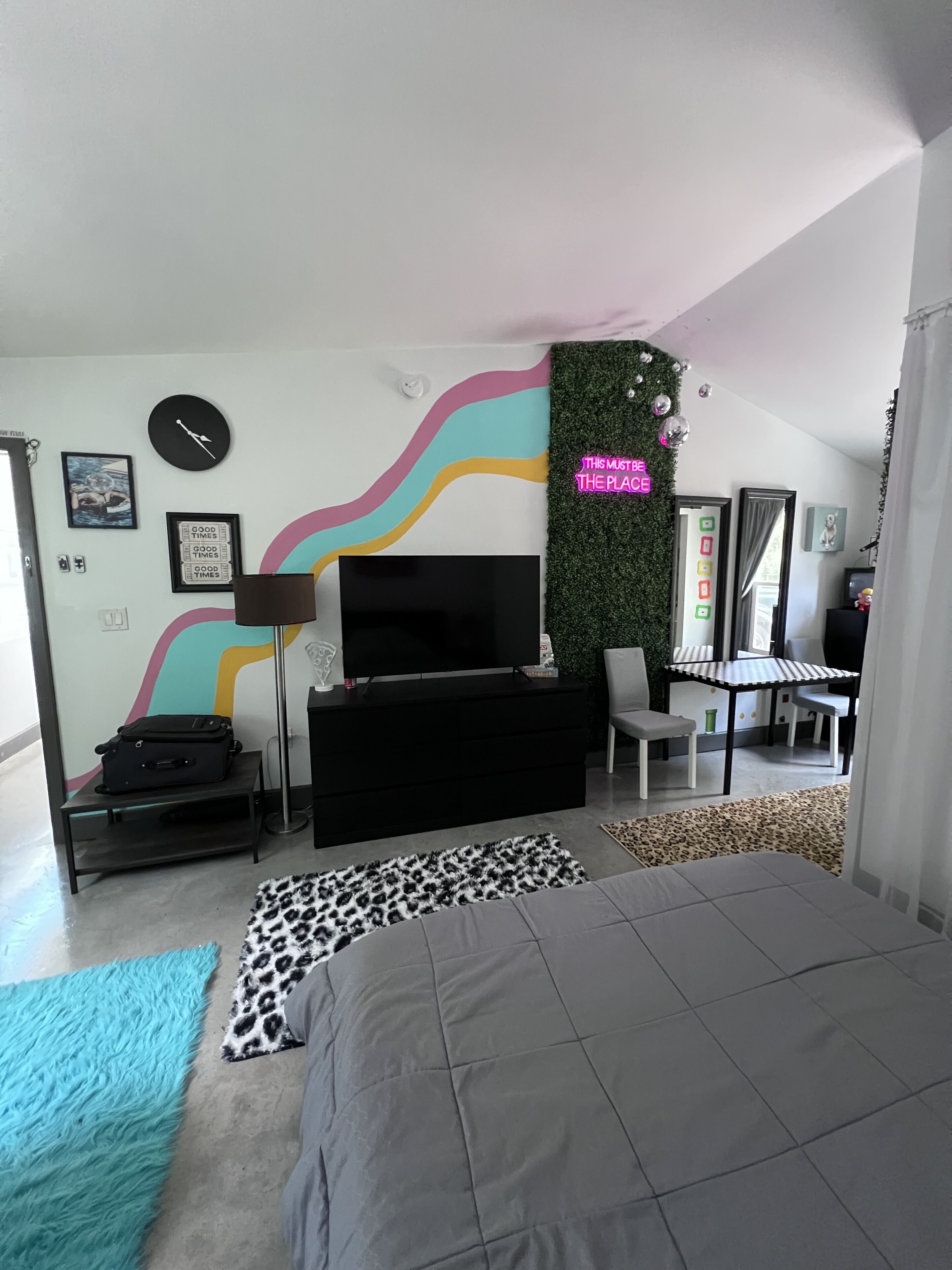 A modern bedroom with a large bed, a TV, a desk, and a neon sign.