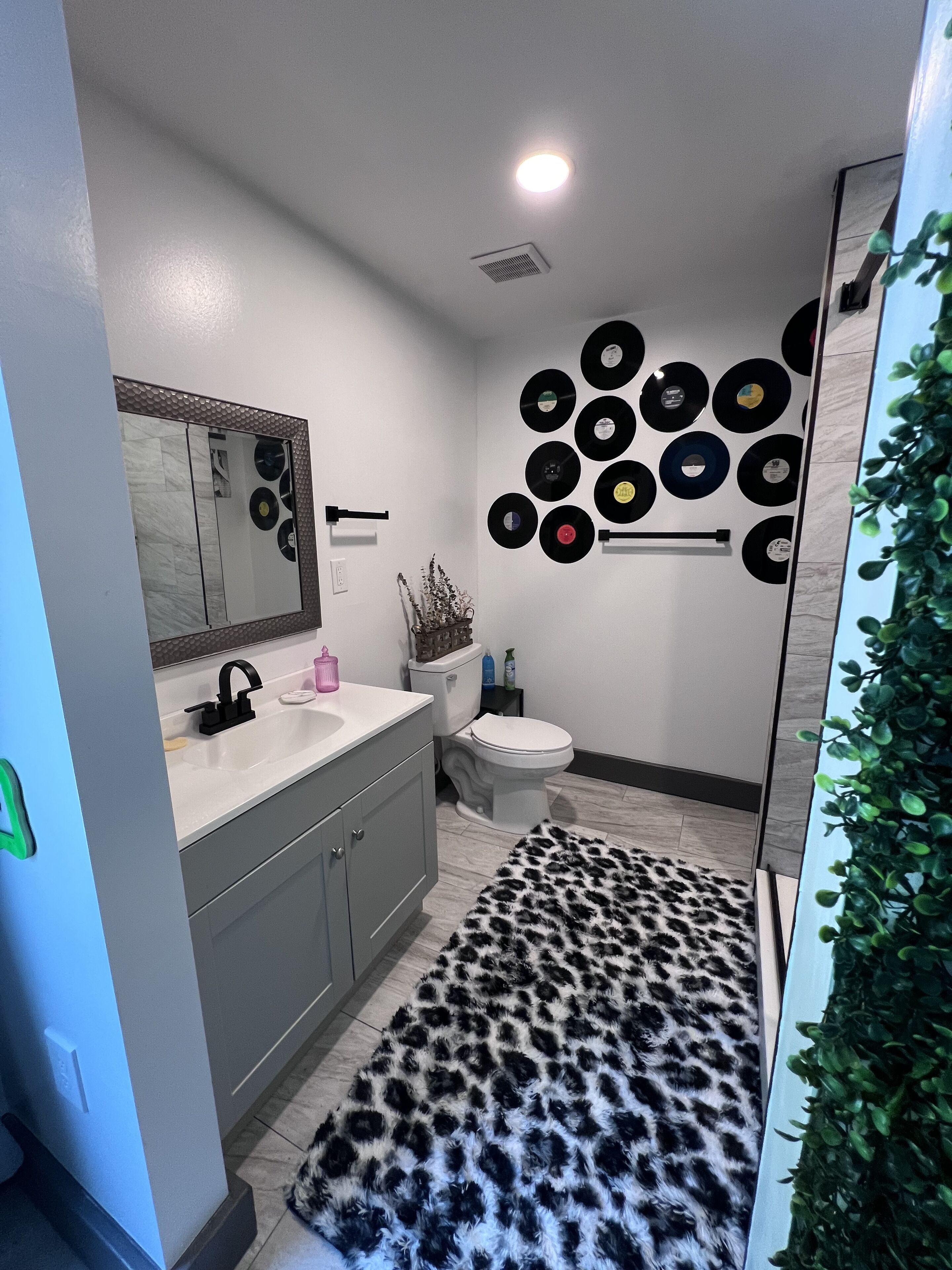 A modern bathroom with a vanity, toilet, and a wall decorated with vinyl records.