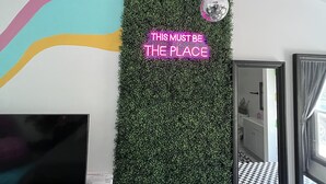 Una habitación con pared verde, un letrero de neón, un televisor de pantalla plana y suelo a cuadros.