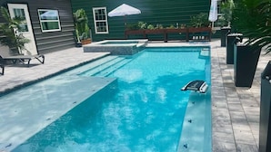 Piscina rectangular con escalones de acceso, rodeada por un patio con una silla de descanso y una mesita.