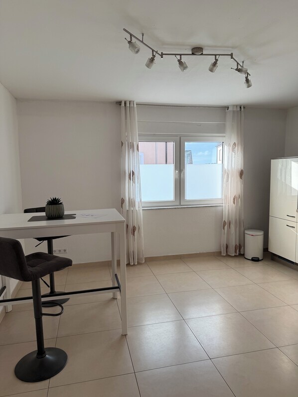 Une pièce comprenant un bureau blanc, une chaise, une plante en pot, une fenêtre avec des rideaux, une armoire blanche et un luminaire au plafond.