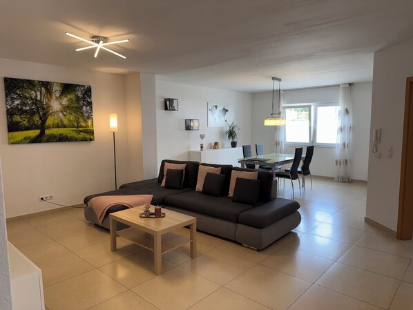 A modern living room with a sectional sofa, a coffee table, and a dining area with a glass table and chairs.