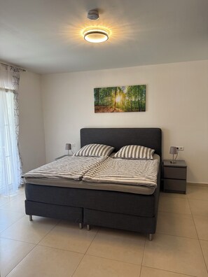A modern bedroom with a large bed, a nightstand, a wall-mounted lamp, and a ceiling light fixture.