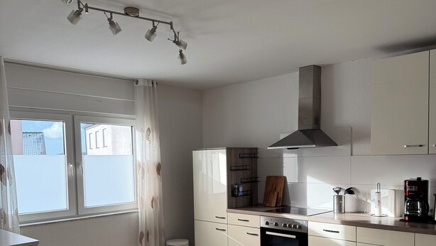 Une cuisine moderne avec des meubles blancs, un four encastré et une fenêtre avec des rideaux.
