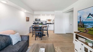 A modern living room with a grey sofa, a wooden coffee table, and a dining area with a round table and chairs. A kitchen with white cabinets and stainless steel appliances is visible in the background. - 211 Walk to the Landing & Convention Center (Branson)