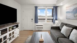 A living room with a flat-screen TV, a grey sofa, a coffee table, a white cabinet, and a window with blue curtains. - 211 Walk to the Landing & Convention Center (Branson)