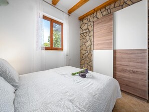 A bedroom with a bed, a stone wall, a wooden door, and a window with curtains. - Relaxing Apartment With sea View and Jacuzzi (Rasa)