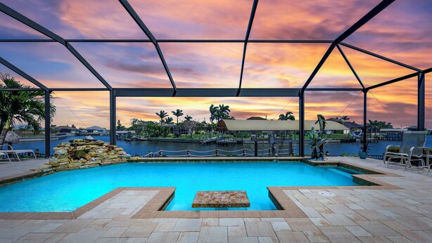 Zwembad met uitzicht op een zonsondergang, omringd door een overdekt terras met stoelen en een stenen muur.