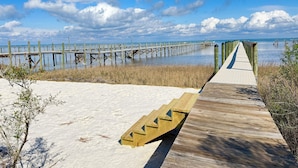 A wooden boardwalk leading to a pier over water, with sand and sparse vegetation in the foreground. - Bayfront oasis with private dock, pool, elevator and easy ADA beach access. (Port St Joe)