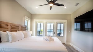 A hotel room with a large bed, a ceiling fan, and a balcony with a view. - Bayfront oasis with private dock, pool, elevator and easy ADA beach access. (Port St Joe)