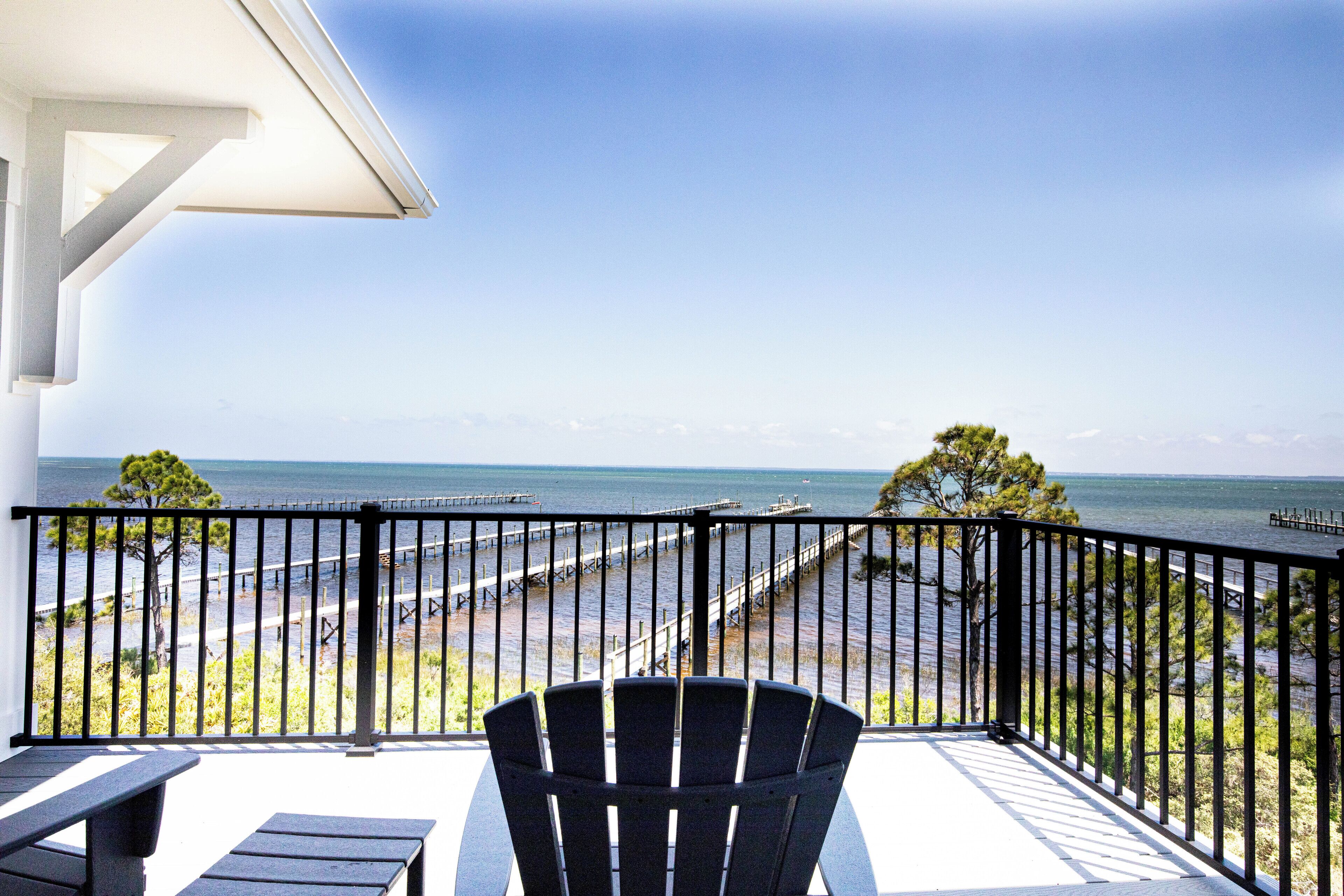 A balcony with a view of the sea, a black chair, and a table.