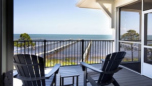 A balcony with two Adirondack chairs and a table, overlooking a pier and the ocean. - Bayfront oasis with private dock, pool, elevator and easy ADA beach access. (Port St Joe)