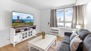A modern living room with a flat-screen TV, a white entertainment unit, a grey sofa, and a large window with curtains. - 207 Walk to Convention Center and The Landing (Branson)
