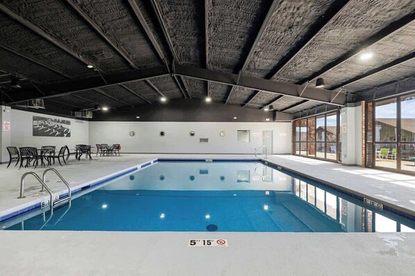 An indoor swimming pool with a clear water surface, a ceiling with exposed beams, and a view of the outside through large windows.