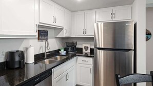 A modern kitchen with white cabinets, a stainless steel refrigerator, a coffee maker, and a sink.