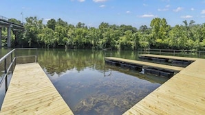 A wooden dock extending into a calm lake, surrounded by lush greenery and a clear blue sky.