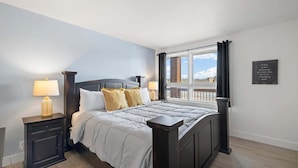 A bedroom with a large bed, two bedside tables, a window with curtains, and a motivational quote on the wall.