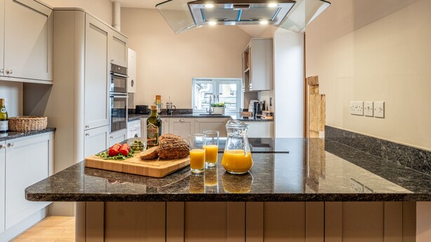 Une cuisine moderne dotée d’un plan de travail en granit, d’un four encastré et d’un luminaire suspendu en verre au plafond.