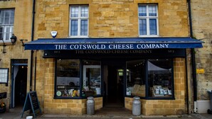 Un bâtiment en pierre surmonté d’une marquise bleue portant l’inscription « The Cotswold Cheese Company ».