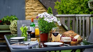 Une table dressée avec une bouteille de vin, un verre de jus de fruits, une plante en pot, une planche de fromages et une miche de pain.