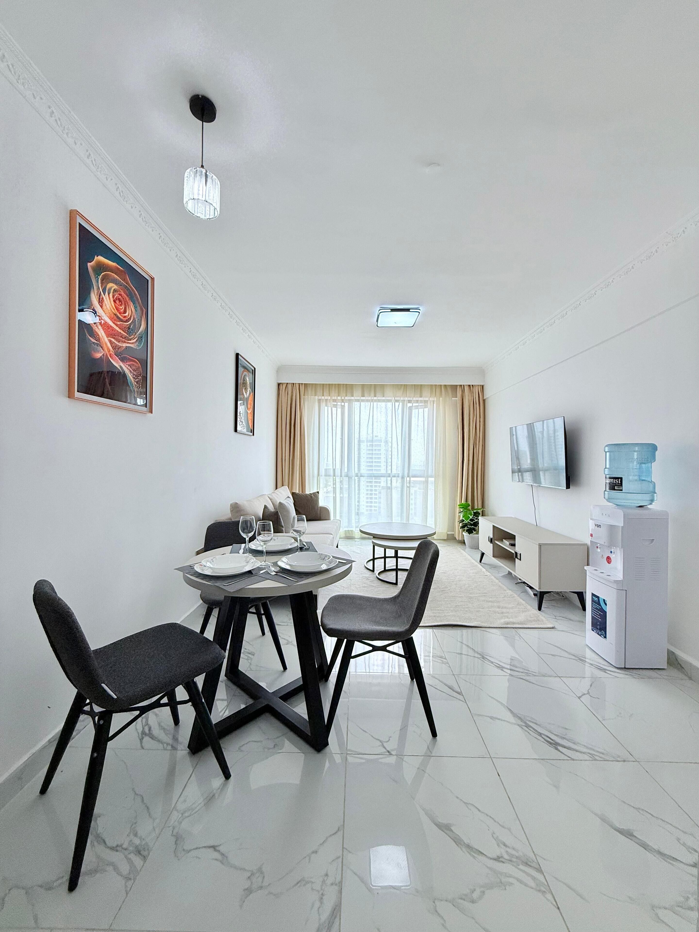 Een moderne woonkamer met een eethoek, een waterdispenser en een flatscreen televisie.