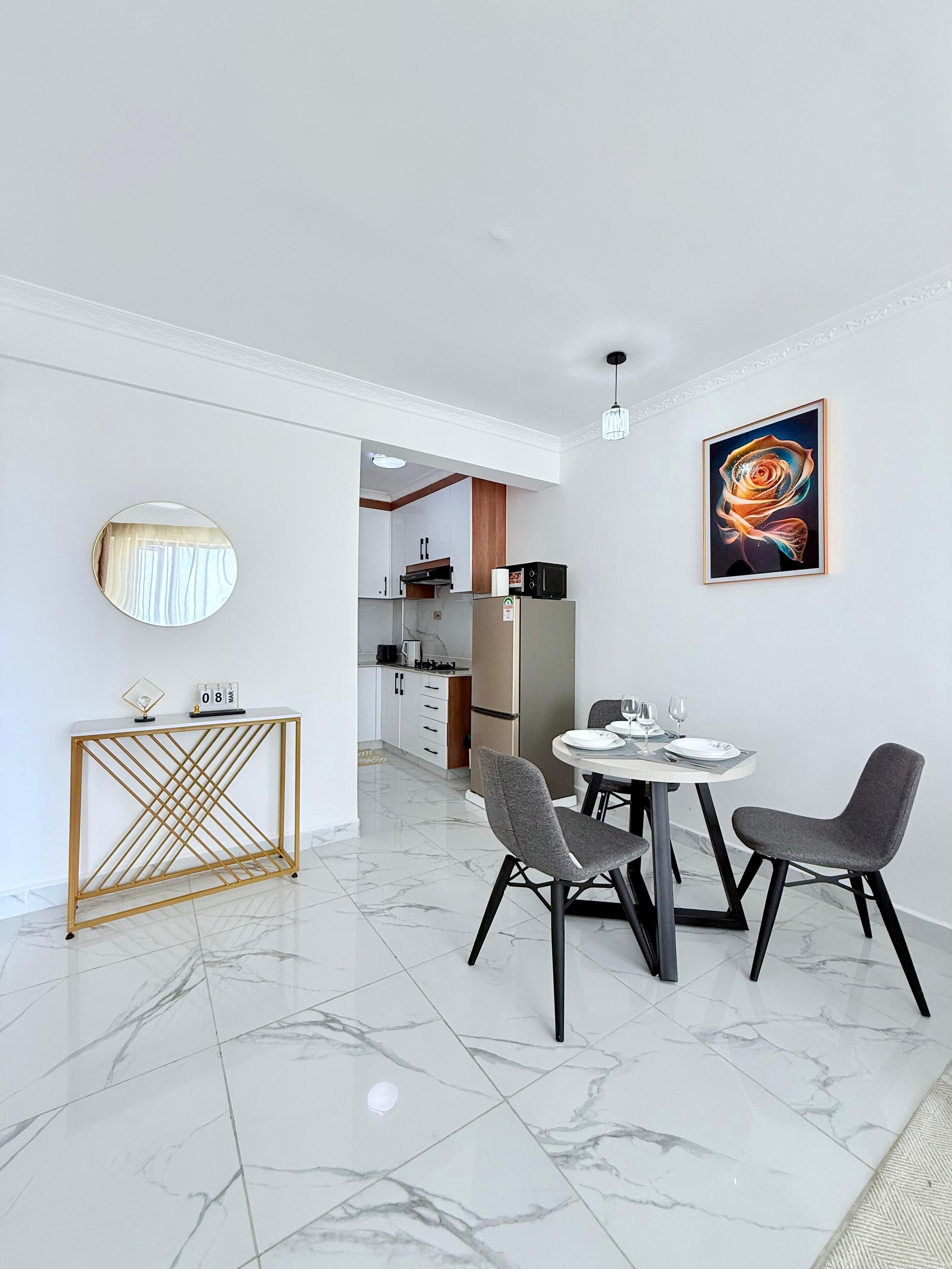 A modern dining area with a marble floor, a round table with two chairs, a decorative console table, a wall-mounted mirror, and a framed artwork.