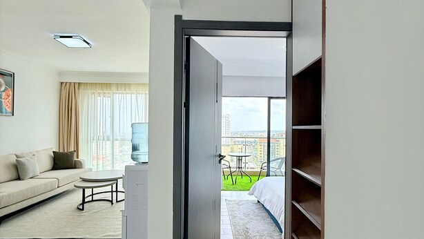 A modern living room with a sofa, coffee table, and a view of a balcony with outdoor furniture. - One Bedroom Apartment in Kilimani, near Yaya Centre (Nairobi)