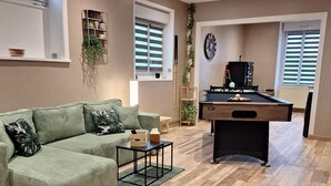 Een woonkamer met een groene bank, een pooltafel en een houten vloer.