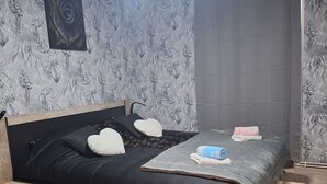Een slaapkamer met een bed, nachtkastje, een klein krukje, een rond tapijt en een plafondventilator.