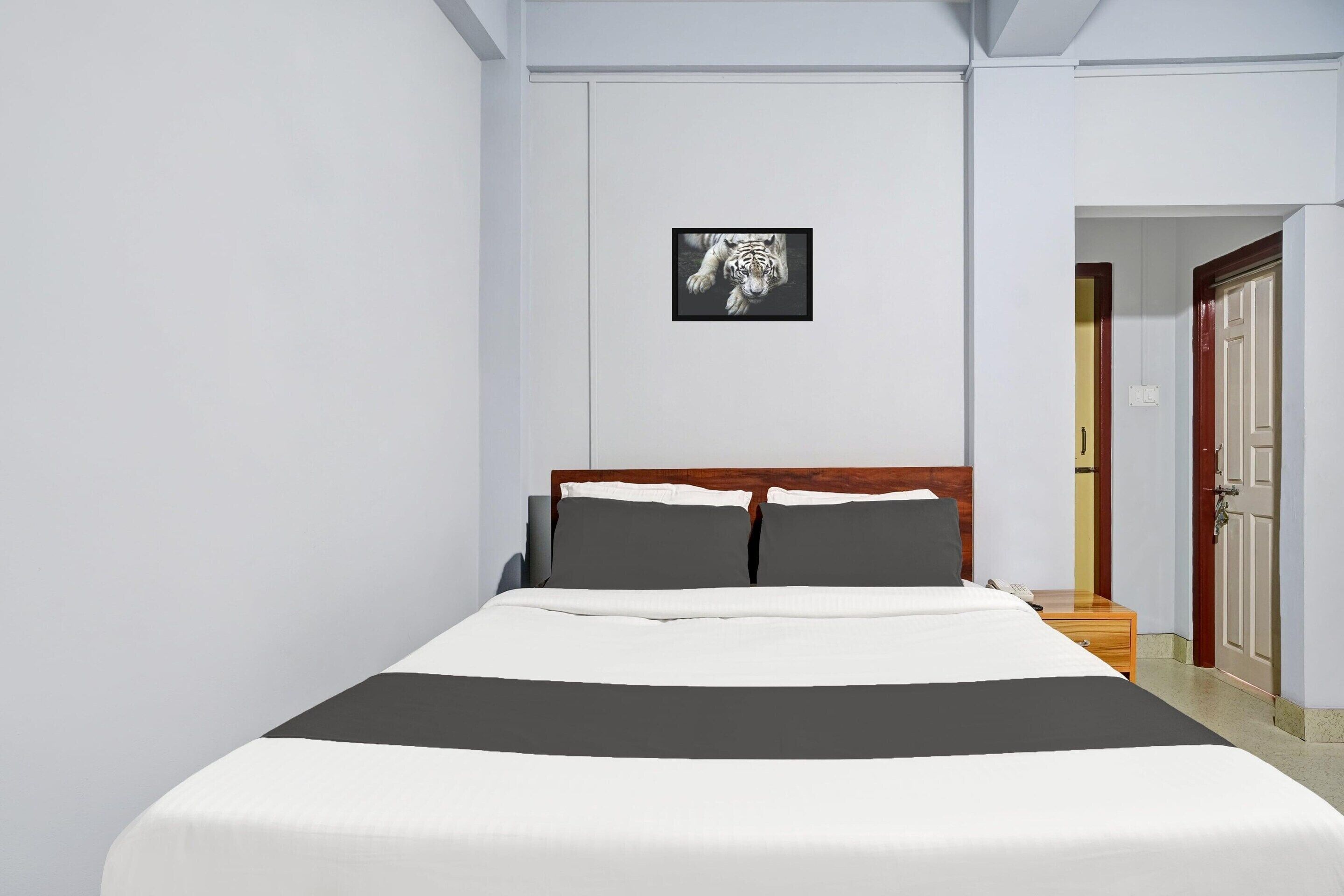 A neatly made bed with a white and gray bedspread, a wooden headboard, and a framed picture of a tiger on the wall.