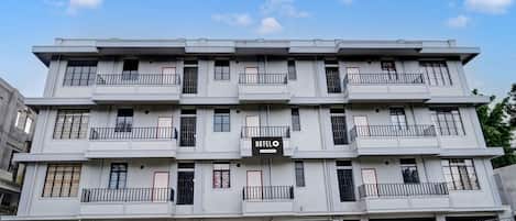 Un hotel de varios pisos con balcones, un letrero que dice "HOTEL" y una cerca de malla metálica al frente.