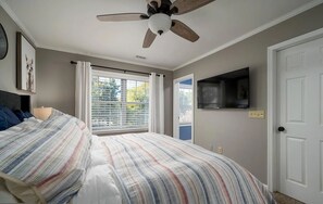A bedroom with a bed, a ceiling fan, a TV mounted on the wall, and a window with blinds.