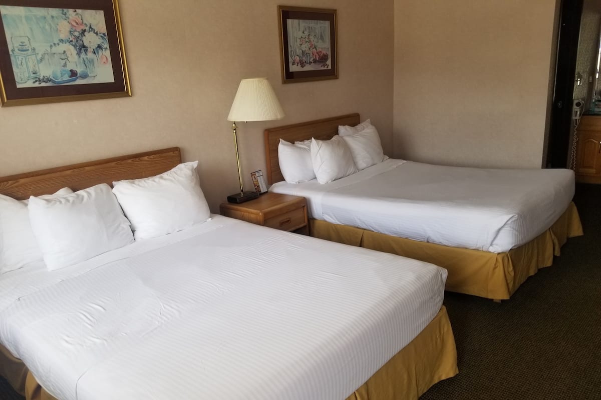 Ein Hotelzimmer mit zwei Betten, einem Nachttisch mit Lampe und zwei gerahmten Kunstwerken an der Wand.
