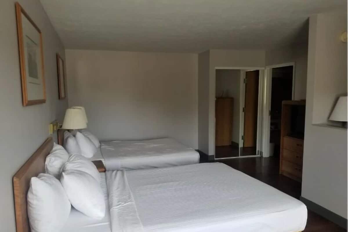 Ein Hotelzimmer mit zwei Einzelbetten, einem Holzkopfteil, einer Nachttischlampe und einem Kleiderschrank.