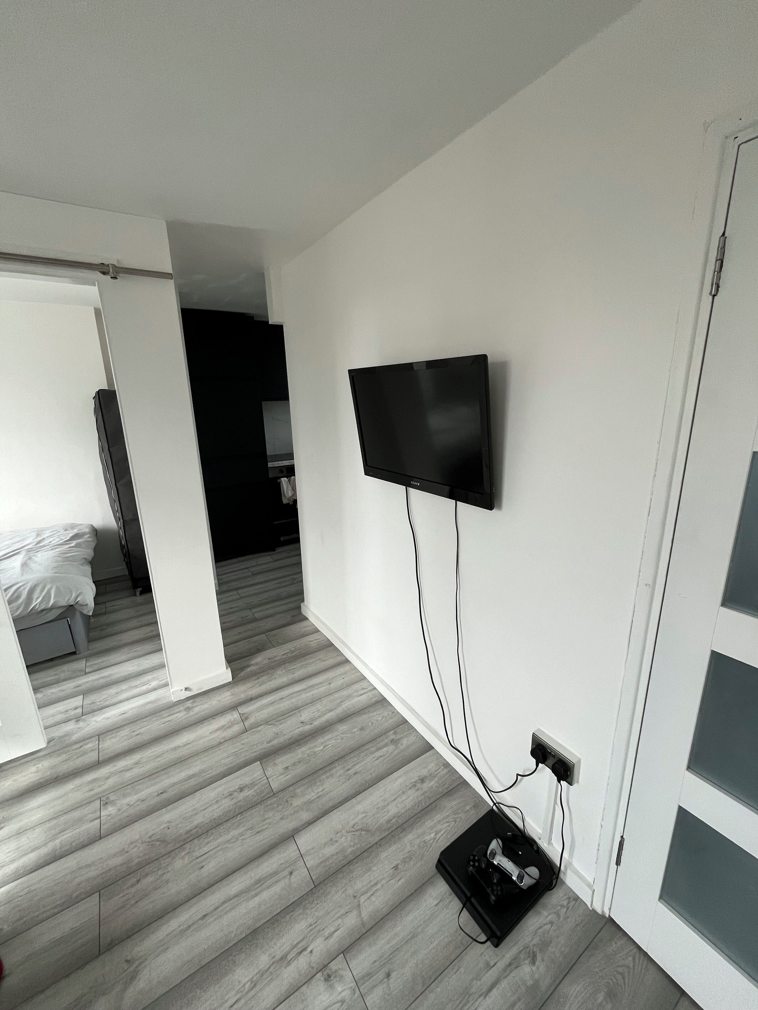 Une pièce dotée d’un téléviseur à écran plat fixé au mur, d’un plancher en bois et d’un lit à l’arrière-plan.