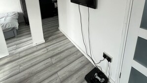 Una habitación con una televisión de pantalla plana en la pared, piso de madera y una cama al fondo.