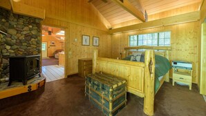 A wooden cabin bedroom with a stone fireplace, a bed, a nightstand, and a small table. - Glen Lake Cabin in the Woods (Eureka)