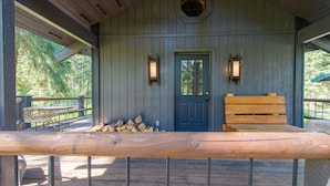 A wooden cabin with a front door, two wall-mounted lanterns, a bench, and a stack of firewood. - Glen Lake Cabin in the Woods (Eureka)