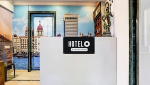 En receptionsdisk med en skylt som visar texten ”HOTELO – företagstjänster” och en väggmålning som föreställer en stadsbild bakom disken.