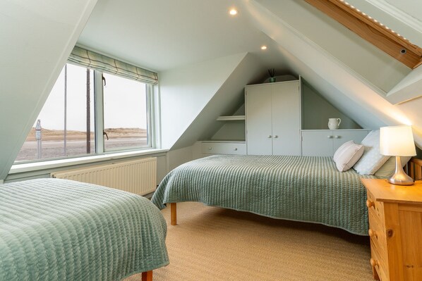 A bedroom with two beds, a wooden dresser, a cabinet, and a window with a view of the beach.