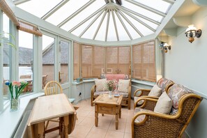 A conservatory with a glass ceiling, wicker furniture, and a view of the outside.