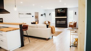 A modern kitchen with a wooden countertop and white cabinets, a dining area with a white sofa and a brown chair, and a living room with a white sofa and a brown chair. - Beautiful, modern, cottage with hot tub and more (Renfrew)