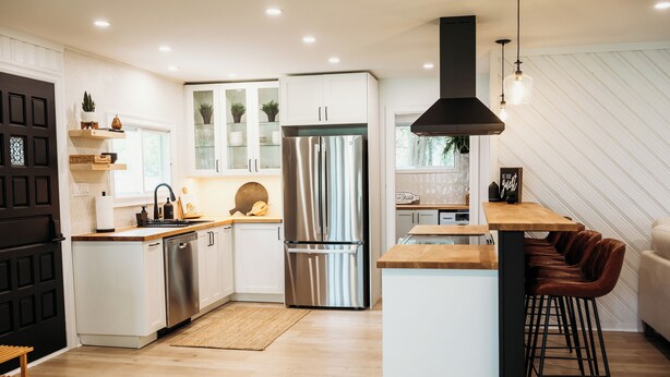 A modern kitchen with white cabinets, stainless steel appliances, and a wooden island with bar stools. - Beautiful, modern, cottage with hot tub and more (Renfrew)