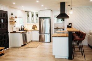 A modern kitchen with white cabinets, stainless steel appliances, and a wooden island with bar stools. - Beautiful, modern, cottage with hot tub and more (Renfrew)