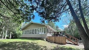 A single-story house with a large windowed front section and a wooden deck. - Beautiful, modern, cottage with hot tub and more (Renfrew)